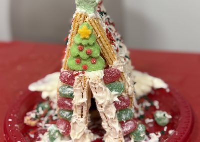 Triangular gingerbread house with colorful candies and icing on a red plate.