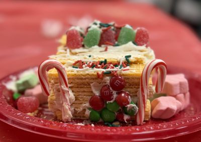 A layered wafer dessert on a red plate, decorated with candy canes, gumdrops, sprinkles, and M&M candies.