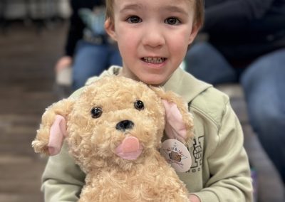 A child holding a fluffy stuffed toy dog with curly light brown fur and pink ears.