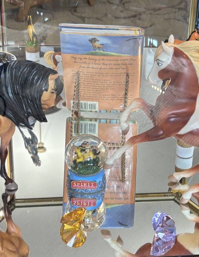 A display case with "Spirit: Stallion of the Cimarron" collectibles including horse figurines, a snow globe, and a book.